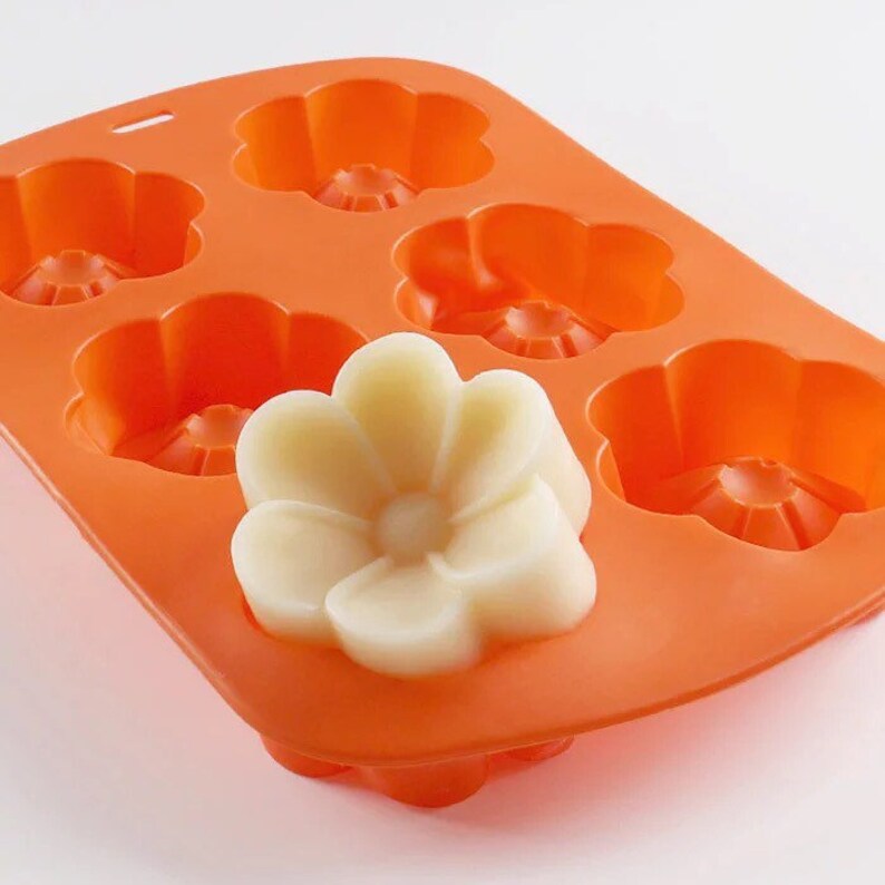 May include: Orange silicone mould with six flower-shaped cavities. A white flower-shaped soap is sitting in one of the cavities.