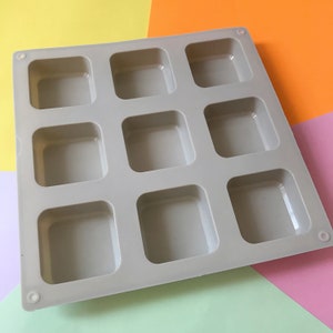May include: A gray silicone mold with nine square cavities. The mold is designed for making small square-shaped items, such as soap, chocolate, or resin crafts.