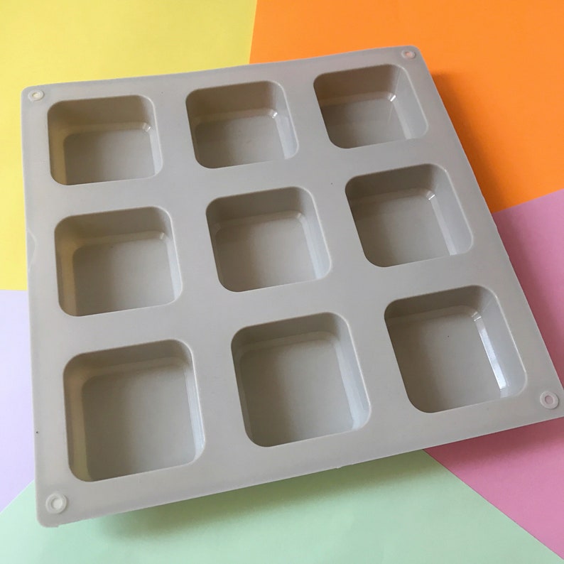 May include: A gray silicone mold with nine square cavities. The mold is designed for making small square-shaped items, such as soap, chocolate, or resin crafts.