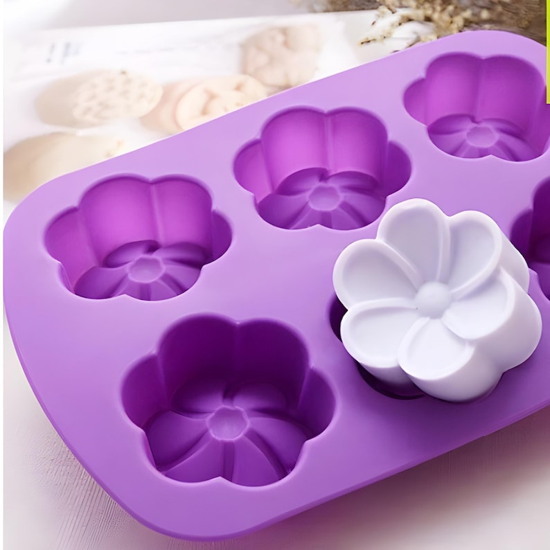 May include: Purple silicone mould with six flower-shaped cavities. A white flower-shaped soap is in one of the cavities.