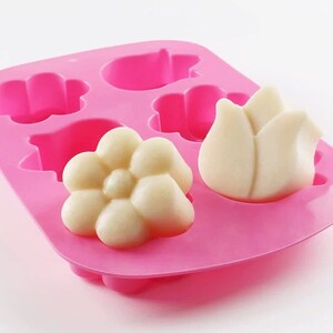 May include: Pink silicone mold with six cavities shaped like flowers and a tulip. The mold is filled with white soap in the shape of a flower and a tulip.
