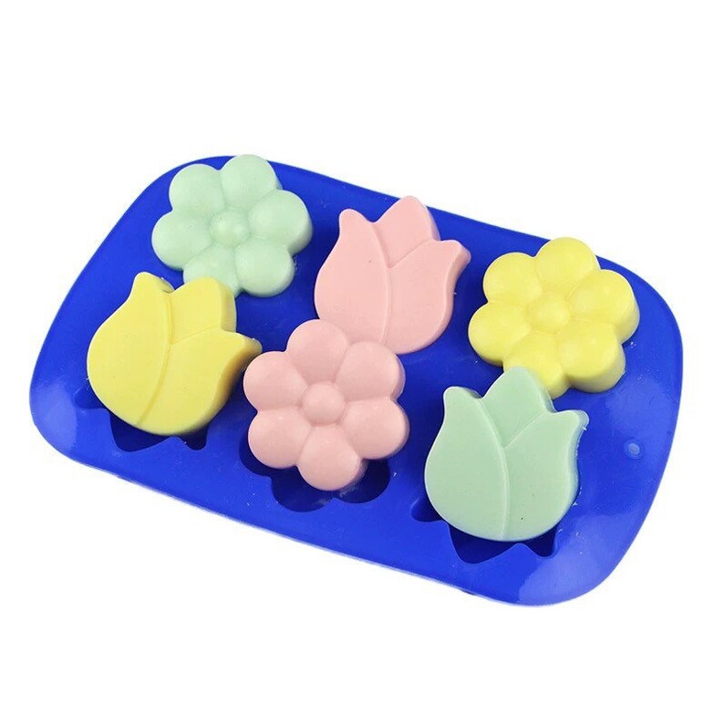 May include: A blue silicone mold with six cavities shaped like flowers and tulips. The mold is filled with colorful soap bars in shades of pink, yellow, and green.