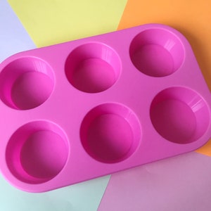 May include: Pink silicone baking mould with six round cavities. The mould is designed for making cupcakes, muffins, or other small treats.
