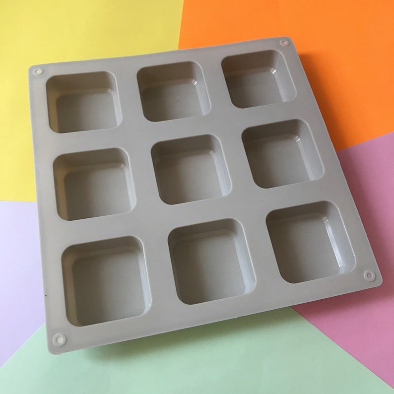 May include: A gray silicone mold with nine square cavities. The mold is designed for making small square-shaped items, such as soap, resin, or chocolate.