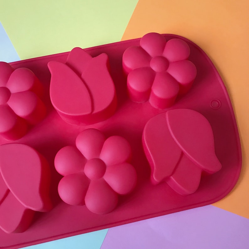 May include: A red silicone mold with six cavities shaped like flowers and tulips. The mold is on a multi-colored background.