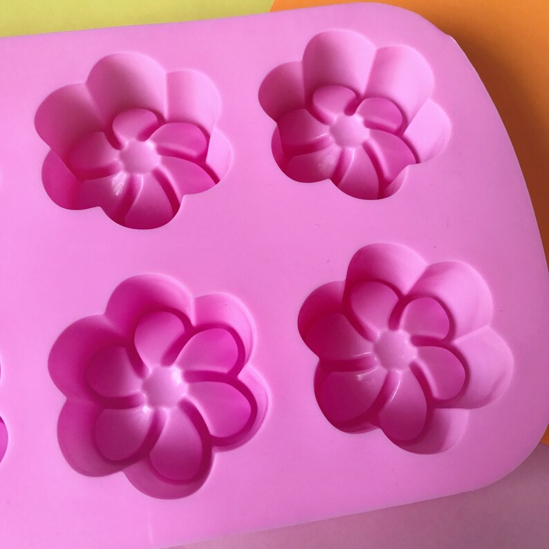 May include: Pink silicone mould with six flower-shaped cavities. The mould is designed for making small cakes, soaps, or other treats.