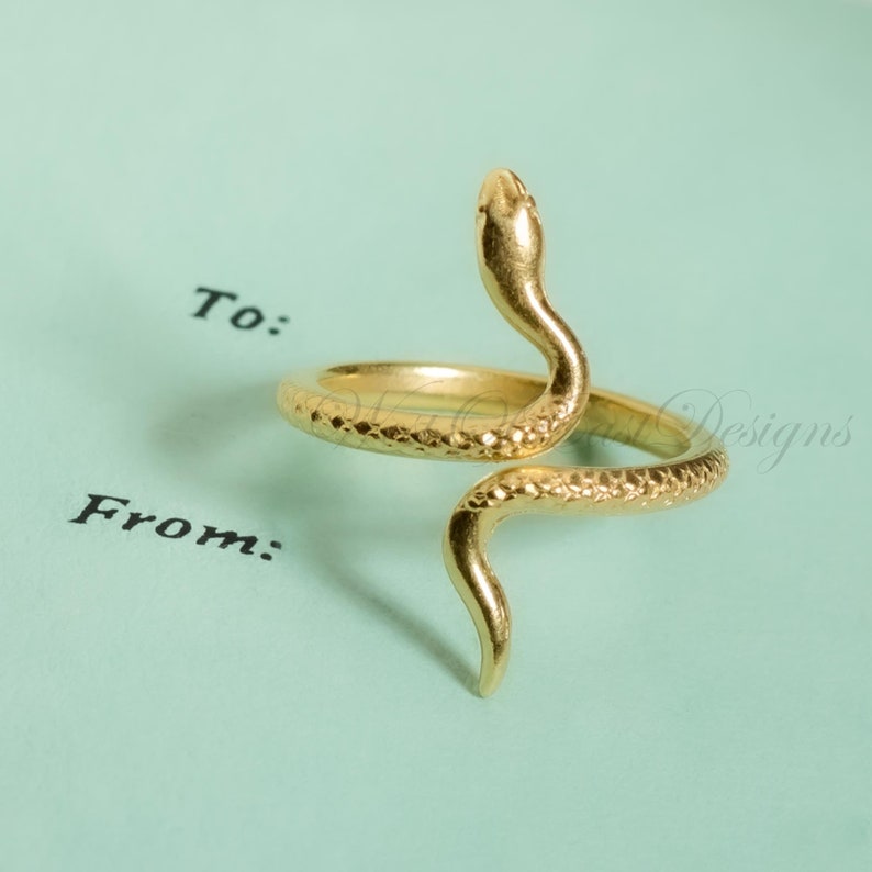 May include: A gold-colored snake ring with a textured surface. The snake's head is raised, and the body coils around the finger. The ring is set against a light blue background with the words "To:" and "From:" printed in black.