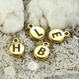 May include: Four gold-colored metal charms with black letter engravings. The letters spell out "H.E.L.B."