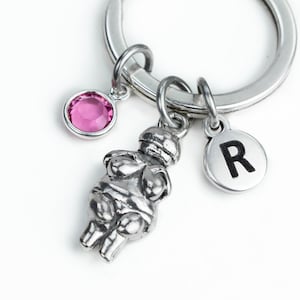 May include: A silver keychain with a small pink crystal charm, a silver charm of a woman, and a silver charm with the letter R.