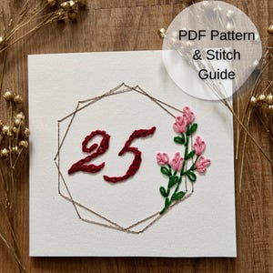 Può includere: Un pezzo di tessuto bianco quadrato con un ricamo a mano del numero 25 in filo rosso scuro, racchiuso in una cornice geometrica color rame. A destra sono ricamati fiori rosa con steli e foglie verdi. Il testo recita PDF Pattern & Stitch Guide.