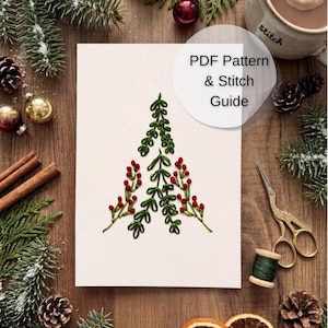 May include: A white card featuring an embroidered Christmas tree design made of green leaves and red berries. The card includes the text PDF Pattern & Stitch Guide. The design is centred on the card, showcasing detailed needlework stitches.