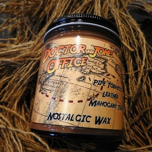 May include: A brown glass jar of "Doctor Jones Office" nostalgic wax. The label features a vintage map design with text indicating "Pipe Tobacco, Leather, Mahogany, Teak". The jar has a black lid and is surrounded by brown twine.