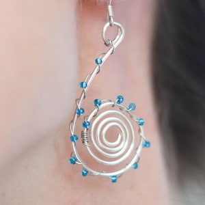 Può includere: Orecchini in filo d'argento con un design a spirale e perline blu.