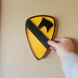 Peut inclure: Un écusson jaune et noir de la 1ère division d'infanterie avec une silhouette de tête de cheval. L'écusson est un insigne militaire traditionnel.