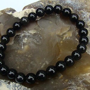 May include: A black beaded bracelet with round, shiny beads. The bracelet is made of natural black onyx stones.