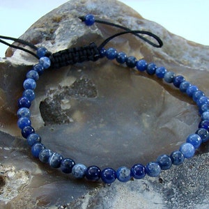 May include: A blue gemstone bracelet with a black cord and adjustable sliding knot closure. The bracelet is made with round, blue gemstone beads.