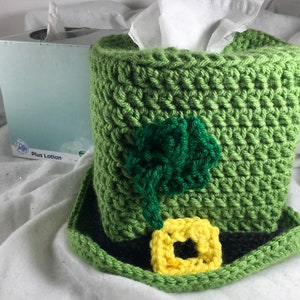 May include: Green crocheted tissue box cover shaped like a leprechaun hat with a black band, a yellow shamrock, and a green shamrock.