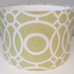 May include: Cylindrical lampshade with a pale green background and a white geometric design. The pattern features interconnected circles and lines. The interior of the lampshade is white.