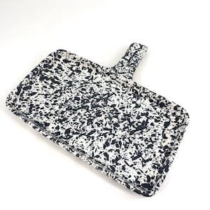 May include: Rectangular serving tray with a handle, white base with a black splatter pattern. The tray's design is a bold contrast, suitable for serving food or as a decorative piece.