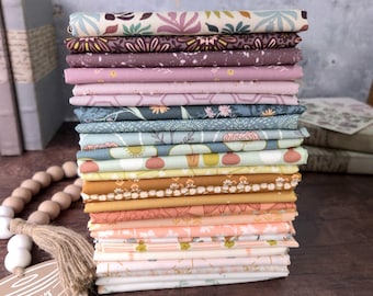 May include: A vertical stack of folded fabric squares featuring a variety of floral and geometric patterns in shades of cream, mauve, dusty blue, mustard yellow, and peach. A wooden spool-shaped tag with the text May your spool always be full.