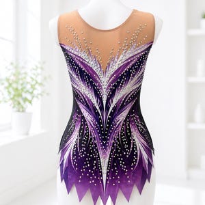 Op de afbeelding: Een mouwloze turnpakje met een nude mesh halslijn en rug. Het turnpakje heeft een zwarte basis met een paars en wit veermotief, versierd met verspreide strass-steentjes. De onderste rand heeft een gekartelde, paarse rand.