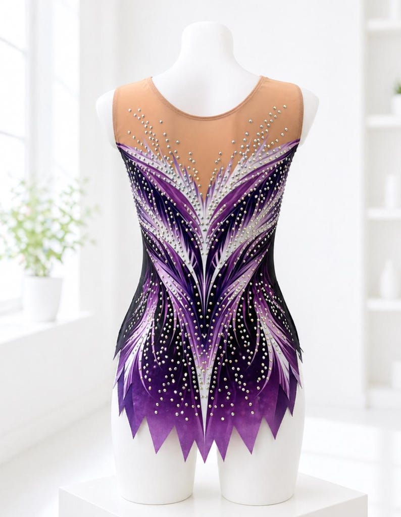 Op de afbeelding: Een mouwloze turnpakje met een nude mesh halslijn en rug. Het turnpakje heeft een zwarte basis met een paars en wit veermotief, versierd met verspreide strass-steentjes. De onderste rand heeft een gekartelde, paarse rand.