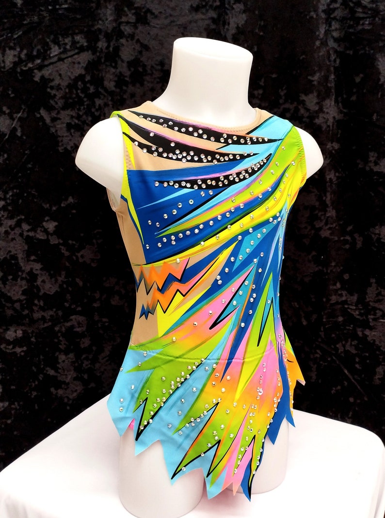 May include: A colorful gymnastics leotard on a mannequin. The leotard features a vibrant design with blue, green, yellow, and pink accents, embellished with sparkling rhinestones. The sleeveless garment has a high neckline and a unique, jagged hemline.