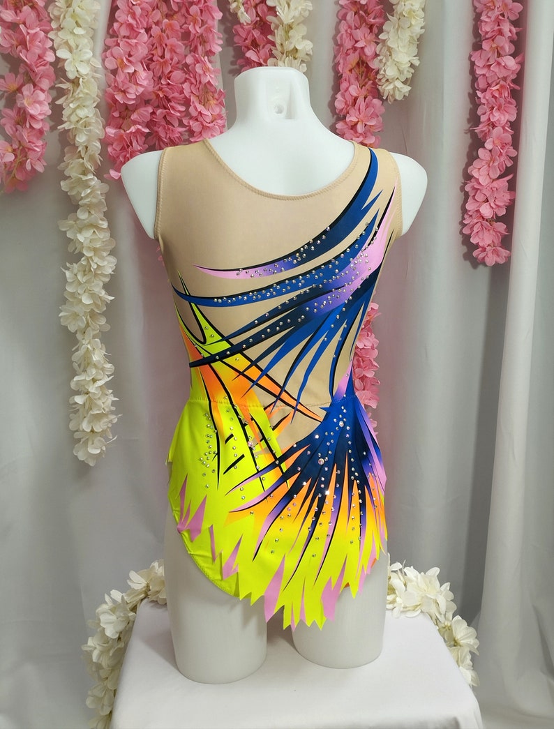 May include: A yellow, pink, blue, and orange leotard with a geometric design. The leotard has a scoop neck and a sleeveless design. The leotard is decorated with rhinestones.