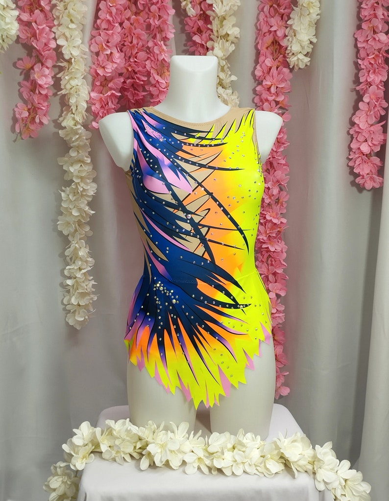 May include: A yellow, pink, blue, and orange leotard with a palm tree print and rhinestones. The leotard has a scoop neck and a sleeveless design.