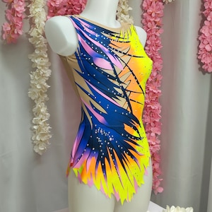 May include: A colorful leotard with a blue, pink, yellow, and orange abstract design. The leotard has a scoop neck and a sleeveless design. It is adorned with rhinestones.