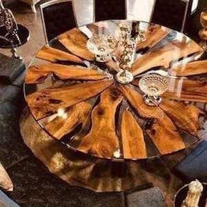 Peut inclure: Vue aérienne d'une table à manger ronde avec un plateau en verre transparent et un design unique en grain de bois. La table est entourée de chaises noires et d'un canapé incurvé. Des objets décoratifs sont placés sur la table.