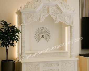 May include: White, intricately carved wooden temple with a peacock design and the Om symbol. The temple features a cabinet with drawers and a decorative floral pattern. The design includes a canopy and pillars. The website address is visible on the side.