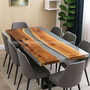 May include: A rectangular dining table with a wooden top and a clear epoxy resin center. The table is surrounded by six gray upholstered chairs with black metal legs. The table measures approximately 72 inches long.