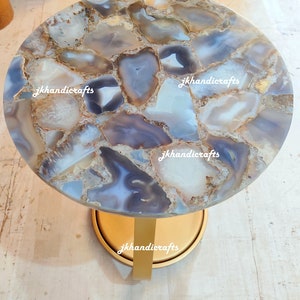 May include: A circular side table featuring a mosaic agate stone top in white, grey, and blue hues. It has a gold-coloured base and a single gold-coloured leg. The text "jkhandicrafts" is printed on the table.