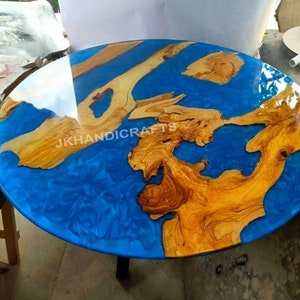 Puede incluir: Mesa redonda de madera con un vibrante centro de resina epoxi azul. La mesa presenta patrones de vetas de madera natural en tonos marrones y beige, con el texto "JKHANDICRAFTS" visible en la superficie.