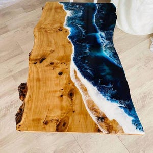 Può includere: Tavolo rettangolare in legno con design a bordo vivo. Il tavolo presenta un design in resina epossidica a tema spiaggia con sfumature di blu, bianco e beige. Le dimensioni del tavolo sono di circa 122 cm di lunghezza e 61 cm di larghezza.