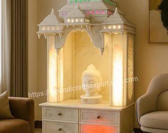 May include: A white marble temple with a tiered roof, illuminated with colorful lights. The temple features a Buddha statue inside and a cabinet with drawers. The image includes the text "https://handicraftsexport.com".