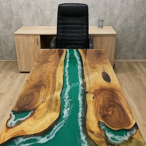 May include: A wooden desk with a river design. The desk has a dark green epoxy resin river running through the middle, framed by natural wood grain. The desk is in an office setting with a black chair and a wooden cabinet.