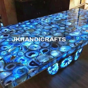 Könnte beinhalten: Ein rechteckiger Tisch mit einer glänzenden Oberfläche aus blauem Achatstein. Der Tisch besteht aus zahlreichen, polierten, oval geformten Steinen in Blau- und Weißtönen. Der Text "JKHANDICRAFTS" ist sichtbar.
