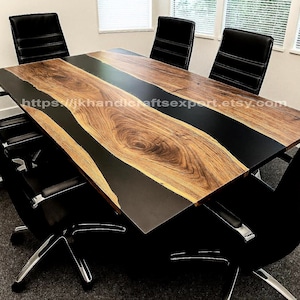 Puede incluir: Una gran mesa de conferencias de madera con un centro de resina epoxi negra. La mesa está rodeada por seis sillas de cuero negro con patas cromadas. La superficie de la mesa tiene un patrón de vetas de madera natural.