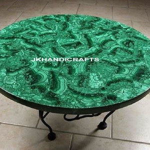 Puede incluir: Una mesa redonda con una tapa de malachite verde y una base de metal negro. La tapa de la mesa tiene un patrón de remolino de verde y negro.