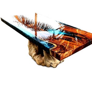Könnte beinhalten: Rechteckiger Holztisch mit einzigartigem Design. Die Tischplatte hat eine natürliche Holzmaserung mit transparentem Epoxidharz, das eine blau-weiße Meereslandschaft erzeugt. Er wird von einem Naturholzsockel getragen.