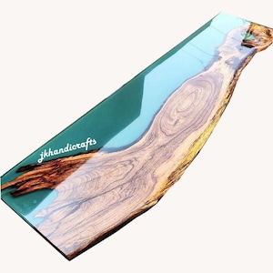 Puede incluir: Tabla de servir rectangular de madera con un diseño de resina epoxi turquesa y azul claro. La veta de la madera es visible, y la tabla tiene el texto "jkhandicrafts". La tabla tiene un borde natural.