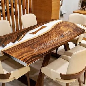 May include: A wooden dining table with a live edge design, featuring a white epoxy resin river. The table is surrounded by six cream-coloured chairs with wooden accents. The table's dimensions are approximately 183 cm long and 91 cm wide.