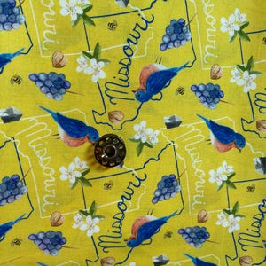 May include: Yellow fabric with a repeating pattern of the state of Missouri, bluebirds, grapes, white flowers, and bees. The text "Missouri" is written in a cursive font.