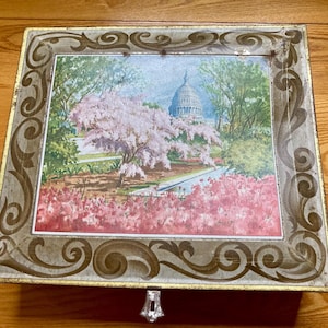 May include: A vintage tin box with a gold and brown ornate border. The box features a painted image of the US Capitol building with cherry blossoms in the foreground.