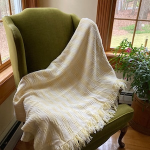 May include: A yellow and white woven throw blanket with fringe on a green armchair. The blanket is draped over the back of the chair and is folded over the seat.