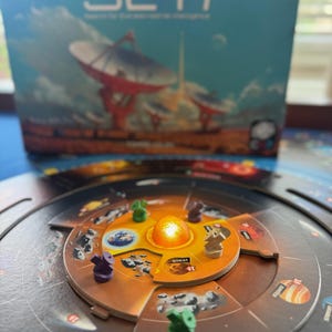 May include: A board game called "SETI: Search for Extraterrestrial Intelligence". The game board shows planets and game pieces. The box art depicts a space scene with satellite dishes. The board has a central sun and planets.
