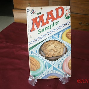 Peut inclure: Une couverture de bande dessinée vintage Mad Magazine Sampler avec une illustration colorée d'une boîte de friandises assorties. La couverture présente le texte "The Mad Sampler" et le numéro "#18".