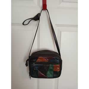 May include: A dark brown leather crossbody bag featuring a patchwork design on the front panel with multi-colored geometric leather segments in shades of blue, green, orange, and dark brown. The bag has a long shoulder strap and zipper closures.